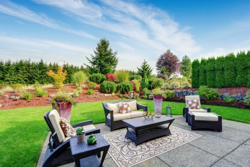 Furniture situated in a well manicured backyard with a table in the middle.