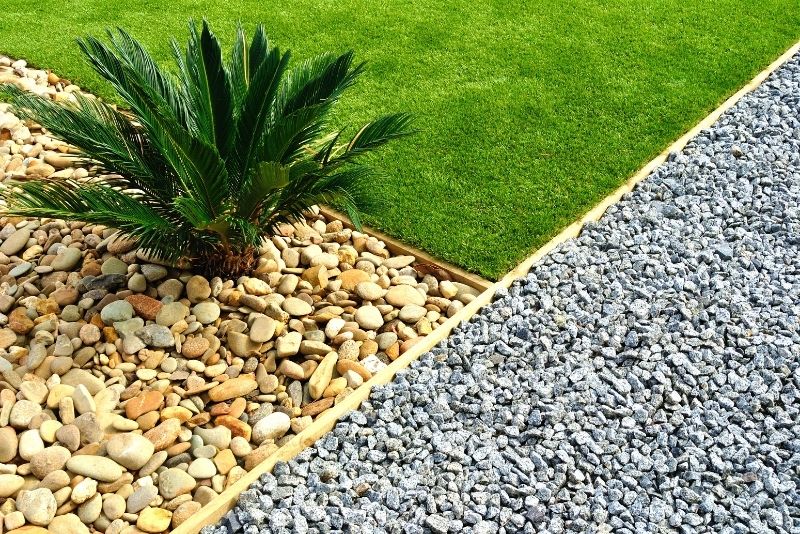 An intersection of grass, gravel and exposed aggregate with a plant in it