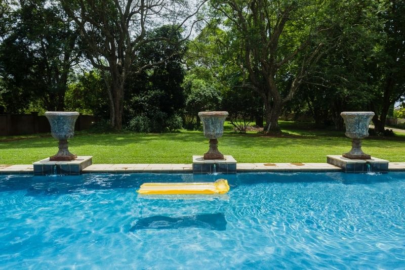 An outdoor pool with grass used for landscaping and beams around it for beautification